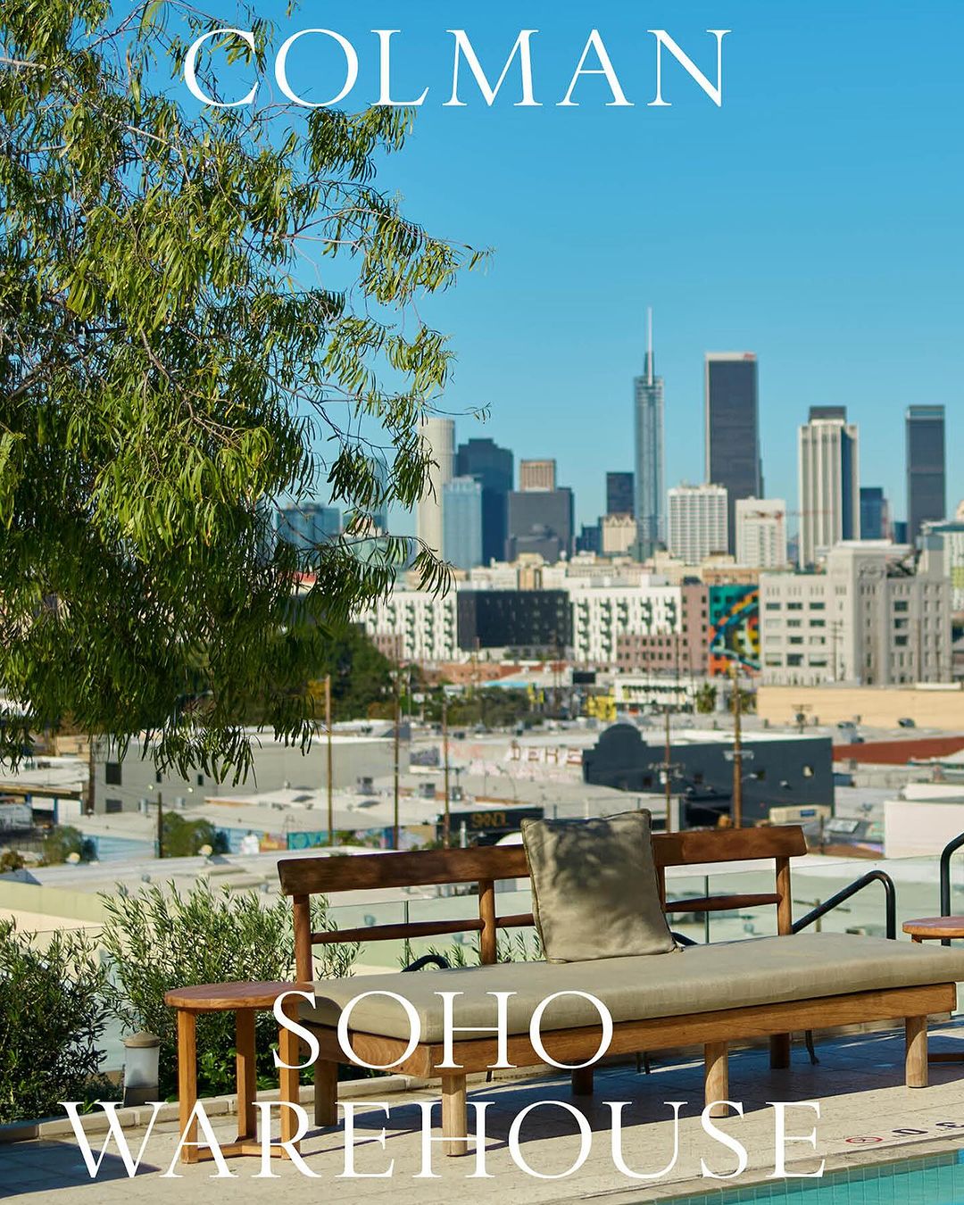 Daybed with a pillow is situated on a deck overlooking a cityscape of Los Angeles, California, with a lush tree in the foreground.