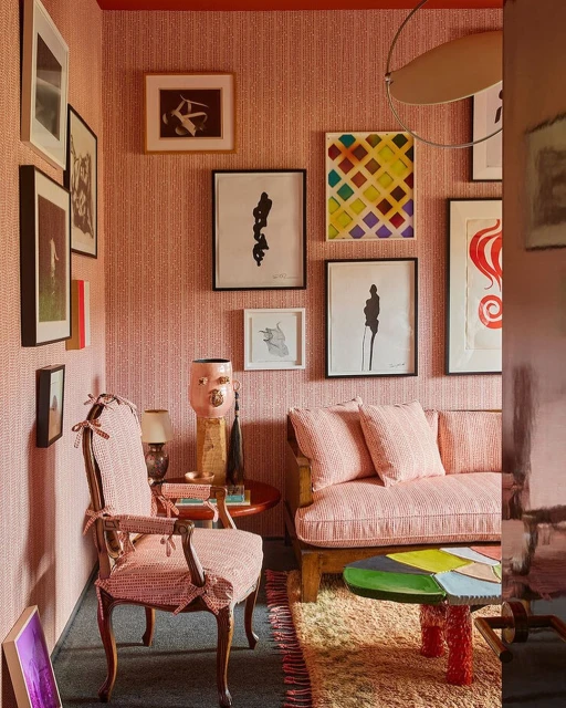 Eclectic living room interior with pink patterned armchair and sofa, colorful artwork, round coffee table, and a patterned rug.