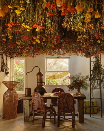 Indoor scene features a dining table with flowers, rustic decor, and dried flowers suspended from the ceiling, creating a warm ambiance.