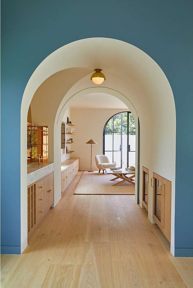 Hallway view through archways into living area. Interior design featuring beige walls, light-colored wood floors, and natural light.