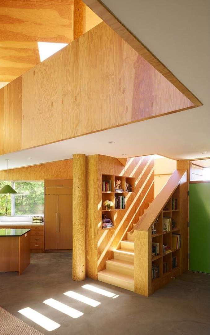 Interior view of a modern home featuring a staircase with built-in bookshelves, wood paneling, and natural light. Modern architectural design.
