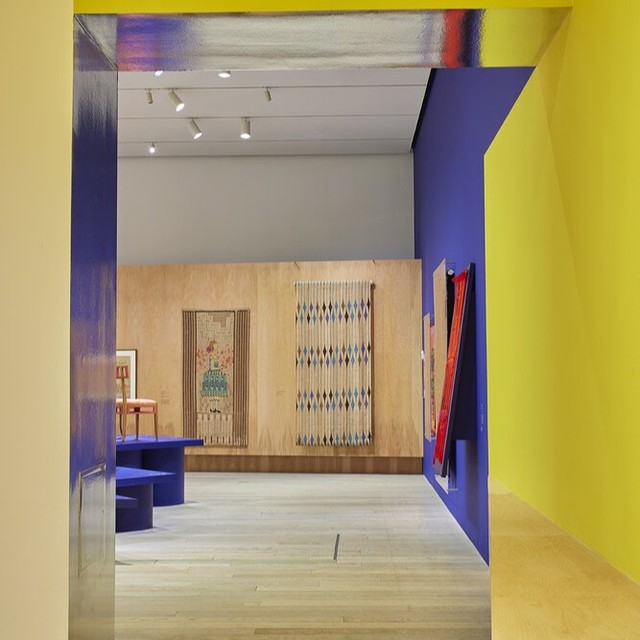 Interior view of a brightly colored art gallery featuring tapestries, paintings, furniture, and colorful walls and trim.