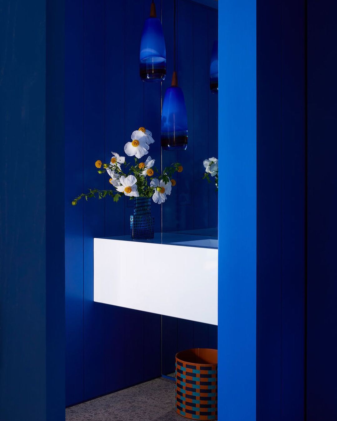 Interior design featuring a white floating vanity, a vase of white flowers, and blue glass pendant lights against a blue wall.