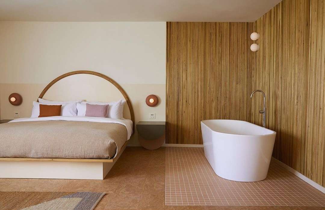 Bedroom and bathroom in a modern hotel suite featuring a platform bed, stylish lighting, minimalist decor, and a standalone bathtub.