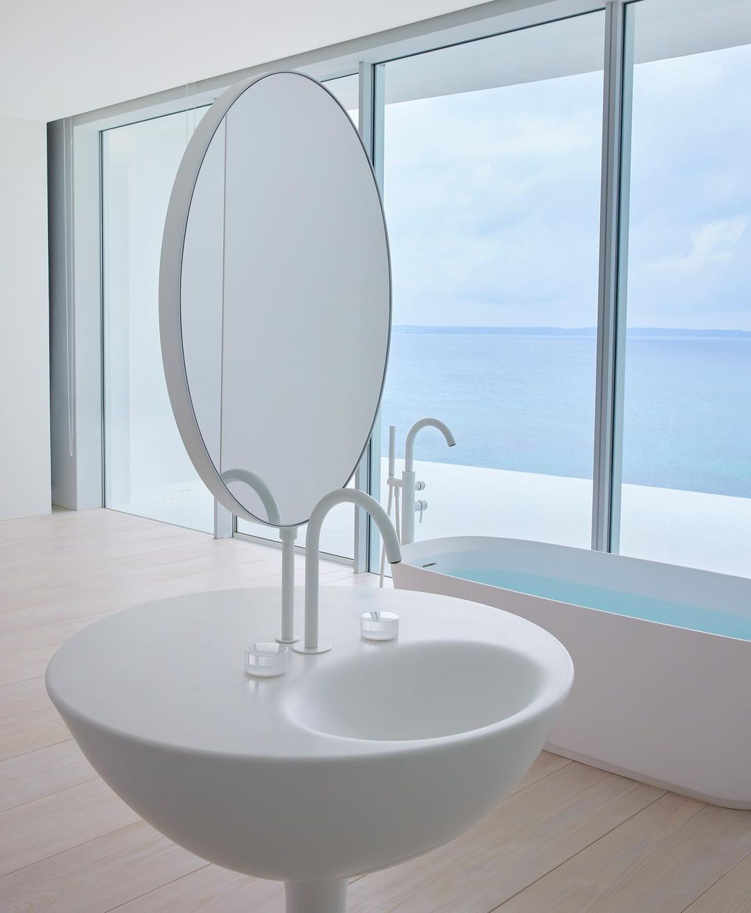 Sleek modern bathroom interior with a unique round sink and mirror, set against a backdrop of large windows overlooking the ocean.
