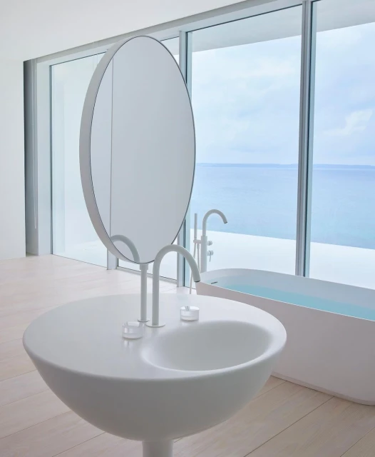 Sleek modern bathroom interior with a unique round sink and mirror, set against a backdrop of large windows overlooking the ocean.
