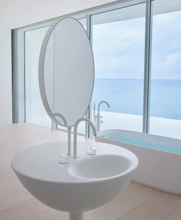 Sleek modern bathroom interior with a unique round sink and mirror, set against a backdrop of large windows overlooking the ocean.