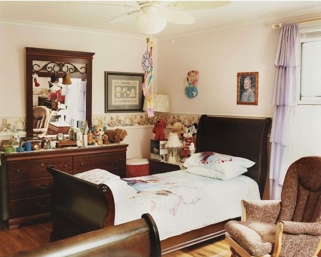 Cozy child's bedroom with a bed, dresser, and armchair. The room is decorated with personal items and has a warm, inviting atmosphere.