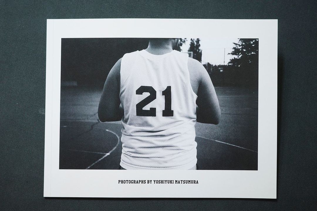 Monochrome photograph of a person in a basketball jersey with the number 21 on the back, captured in a medium shot on an outdoor court.