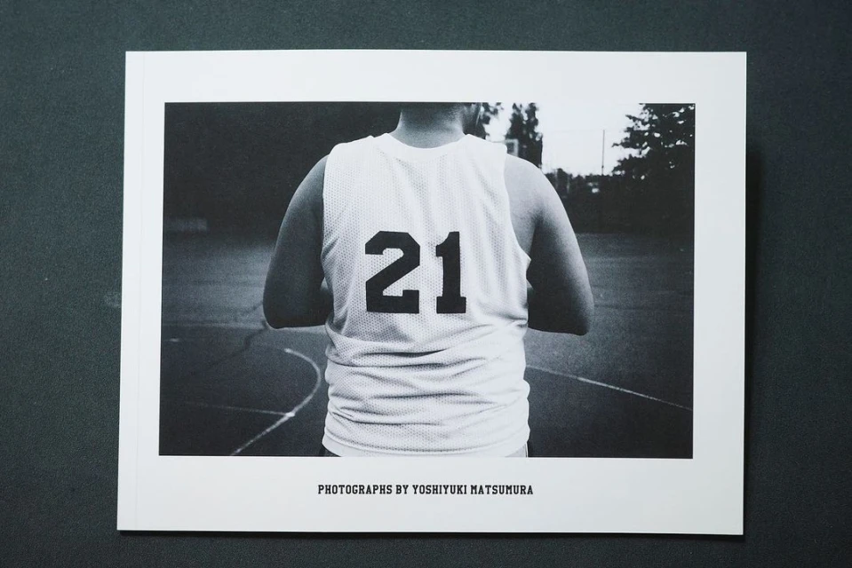 Monochrome photograph of a person in a basketball jersey with the number 21 on the back, captured in a medium shot on an outdoor court.