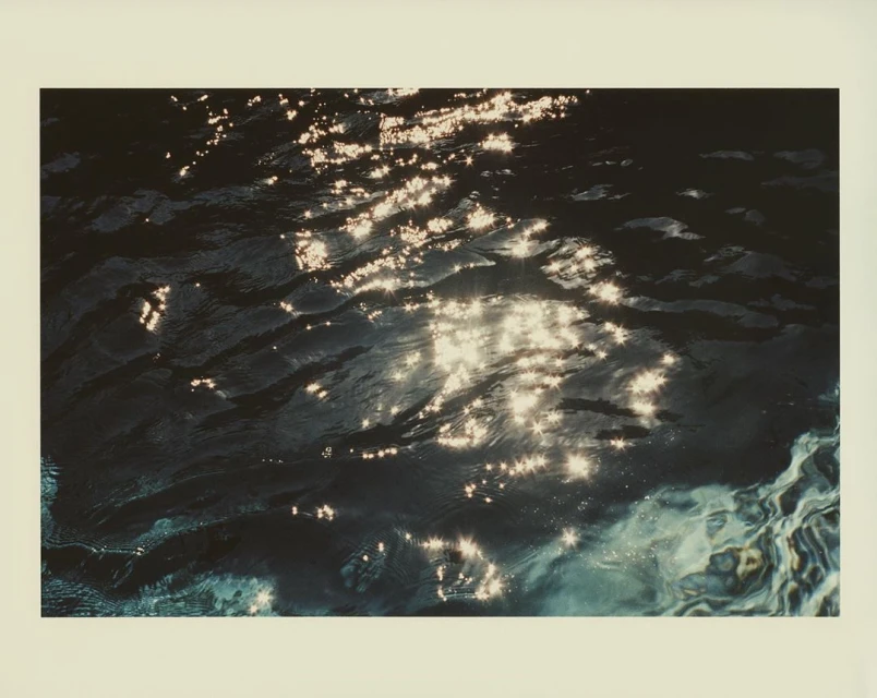 Abstract photography of dark water with bright shimmering sunlight reflections on the surface creating an ethereal, textured effect.