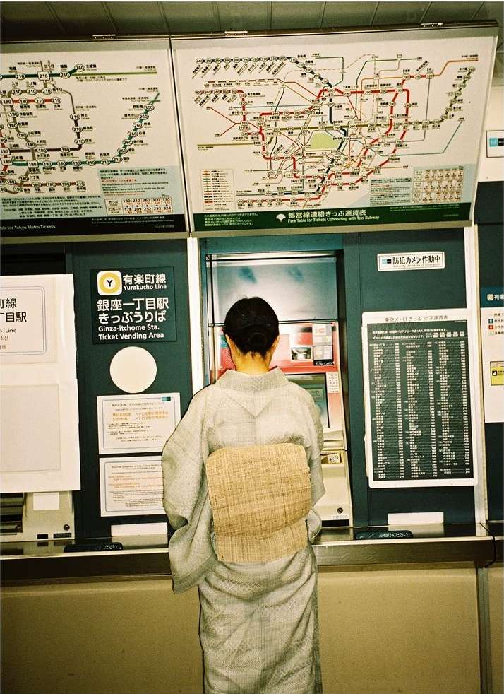 Woman in kimono at subway ticket machine in Japan, reading maps. Inside train station with maps and schedule. Urban transportation.