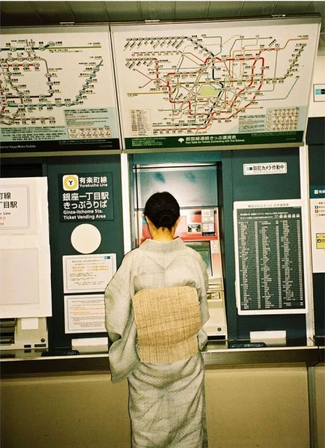 Woman in kimono at subway ticket machine in Japan, reading maps. Inside train station with maps and schedule. Urban transportation.
