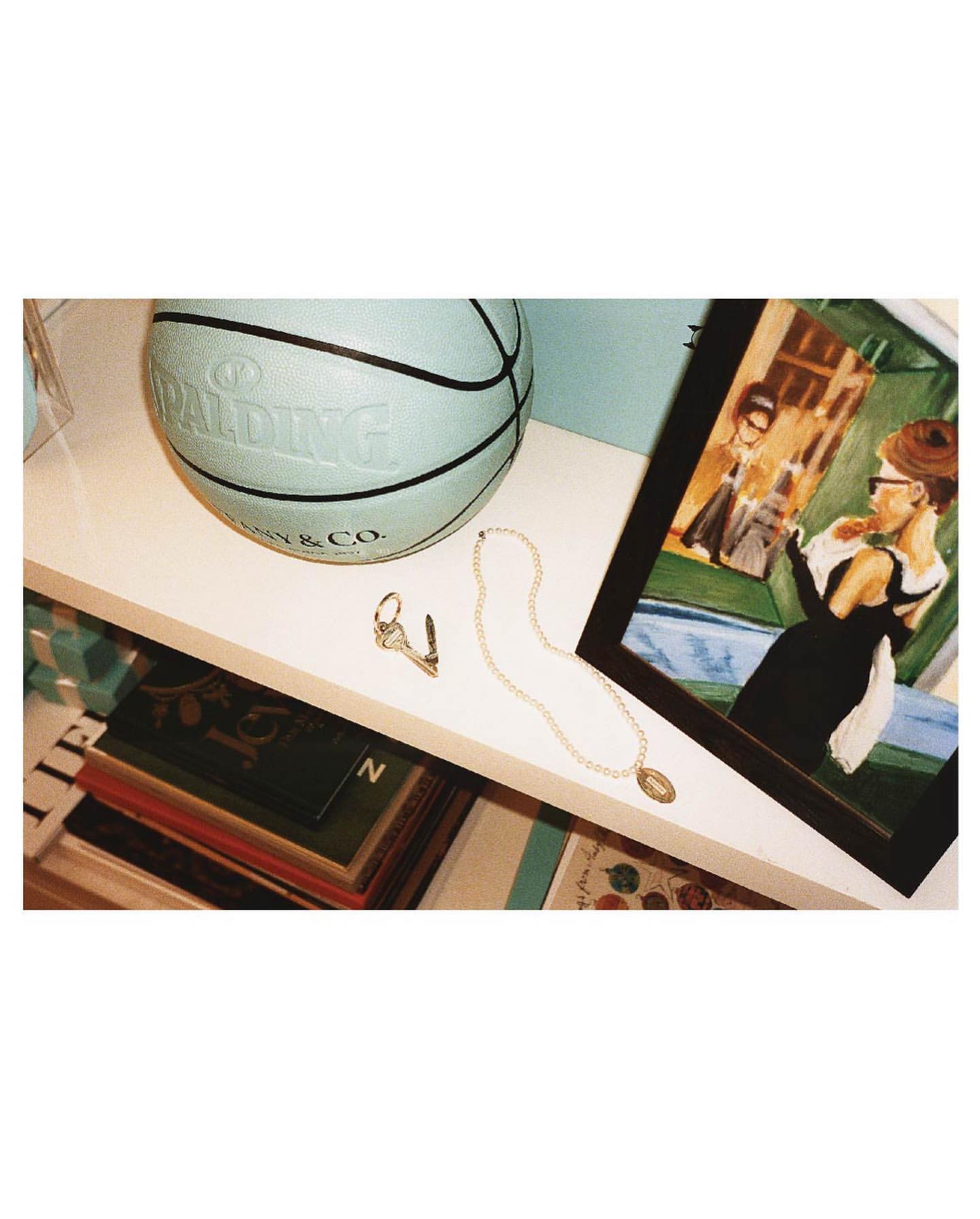 Still-life shelf arrangement featuring a Spalding & Tiffany & Co. basketball, framed artwork, jewelry, and stacked books.
