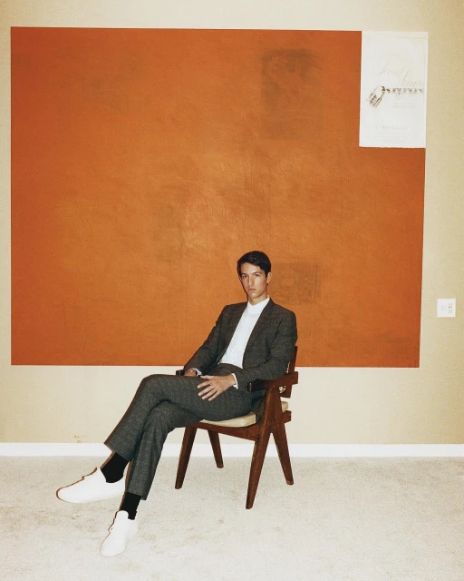 Portrait of a man in a suit sitting on a mid-century modern chair against a large abstract art background.