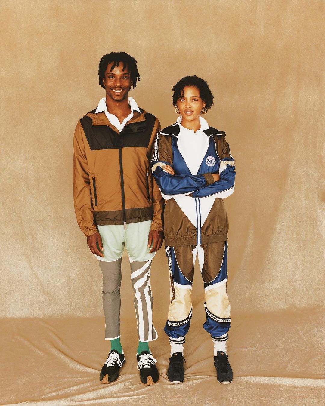 Two fashion models in coordinated sportswear posing against a tan background. The outfits are brown, white, and blue, and black trainers.