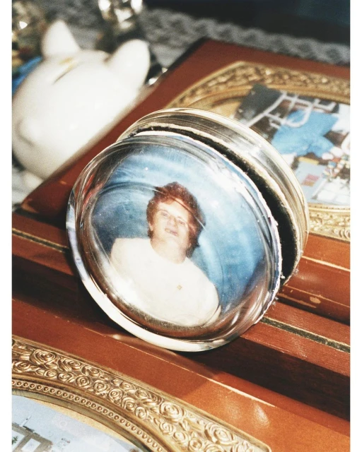 Close-up of a glass paperweight encasing a photograph of a woman in a white shirt, resting on a wooden box with decorative gold trim.