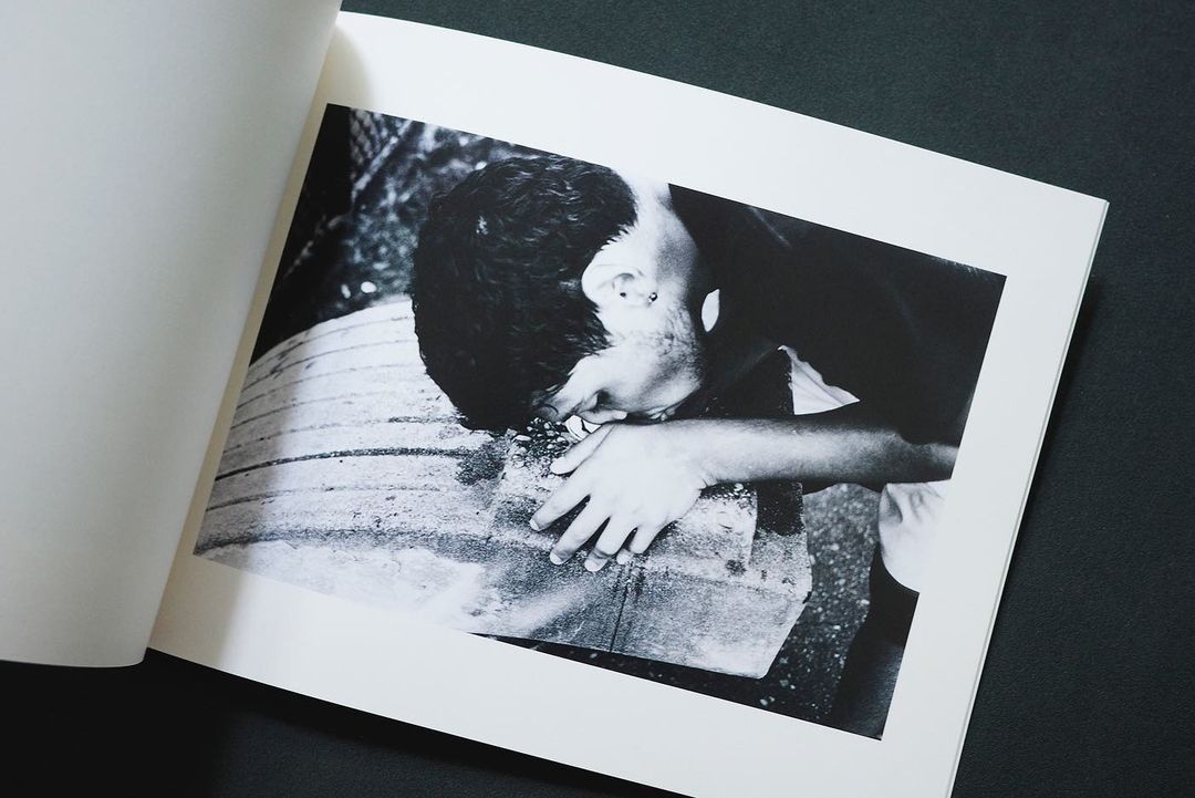 Black and white photograph of a young child drinking from a water fountain as seen within the pages of a photo book.