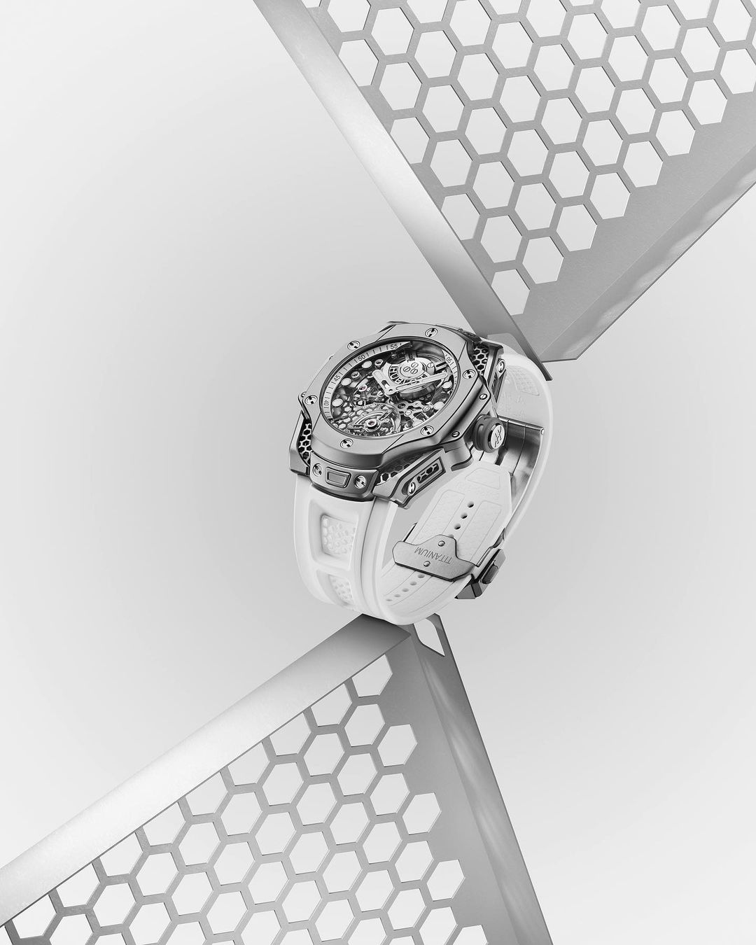 Luxury wristwatch with a white band is elevated by geometrically patterned silver platforms against a stark white background.