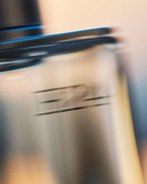 Blurry close-up of a metal water bottle with black accents, showcasing a minimalist design and blurred motion effect in soft lighting.