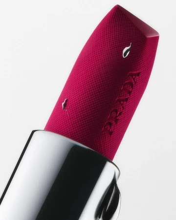 Close-up macro shot of a vibrant pink Prada lipstick with textured surface in a silver case against a white background