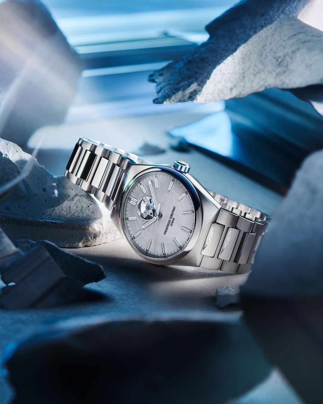 Luxury silver wristwatch with a stainless steel bracelet showcased against a backdrop of textured stones and cool blue lighting.