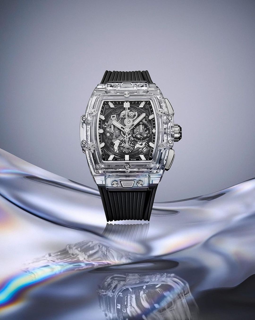 Transparent luxury watch displayed on a reflective surface with a light grey background, showcasing horology and high-end craftsmanship.