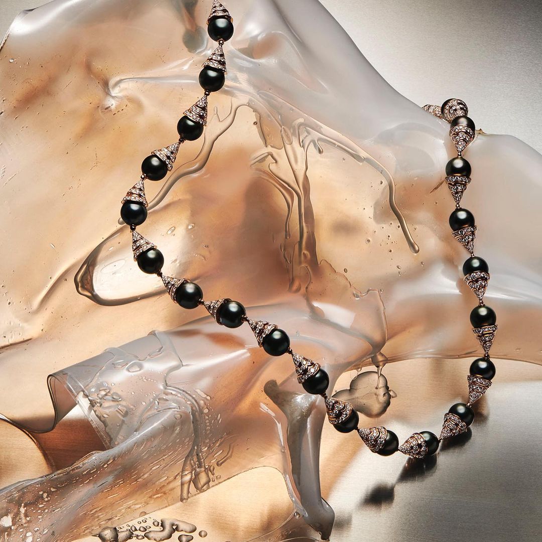 Black pearl necklace with diamond accents on a swirling metallic surface, studio lighting, and elegant jewelry design.