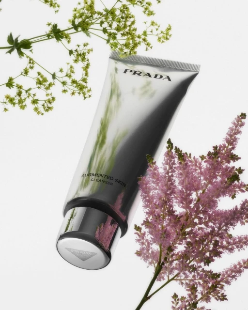 Silver Prada skin cleanser tube surrounded by green and pink flowers against a clean, bright white background in studio lighting.