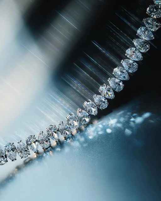 Elegant diamond necklace with pear-shaped stones displayed on a reflective surface, illuminated by soft, directed lighting, showcasing luxury.