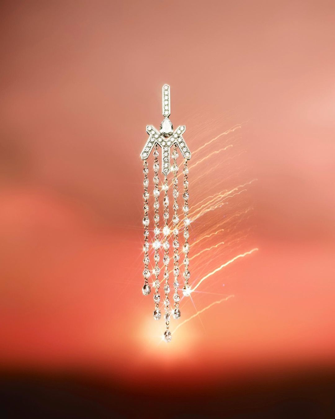 Elegant silver earring with cascading crystals sparkles against a soft orange gradient background, exuding luxury and sophistication.
