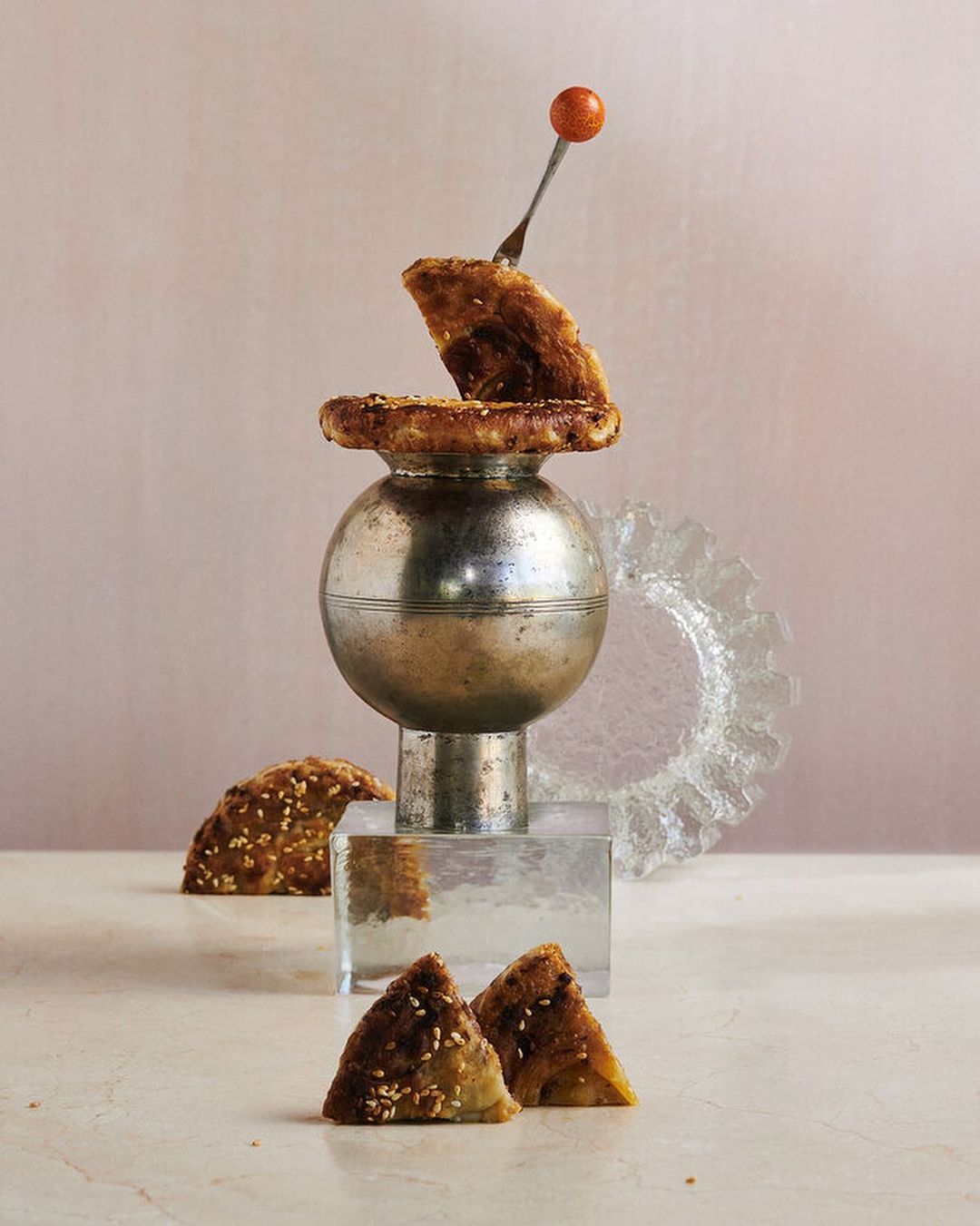 Elevated view of food photography featuring an artistic arrangement of samosas on a marble surface with a pink backdrop and creative props.