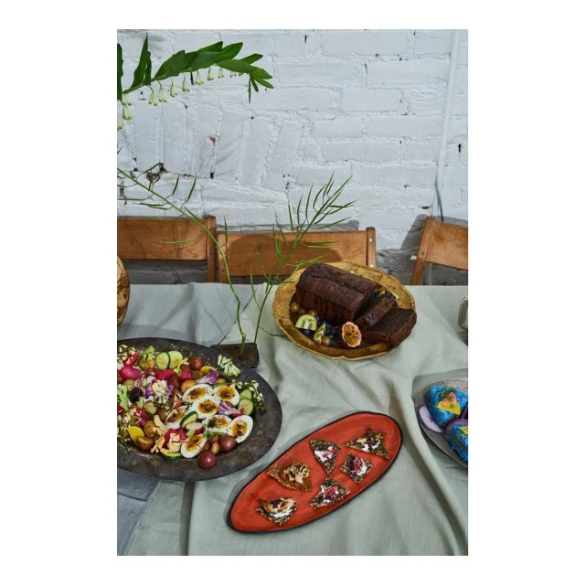 Overhead shot of table featuring loaf of bread, cake slices, salad, and flower arrangement against white brick wall background. 