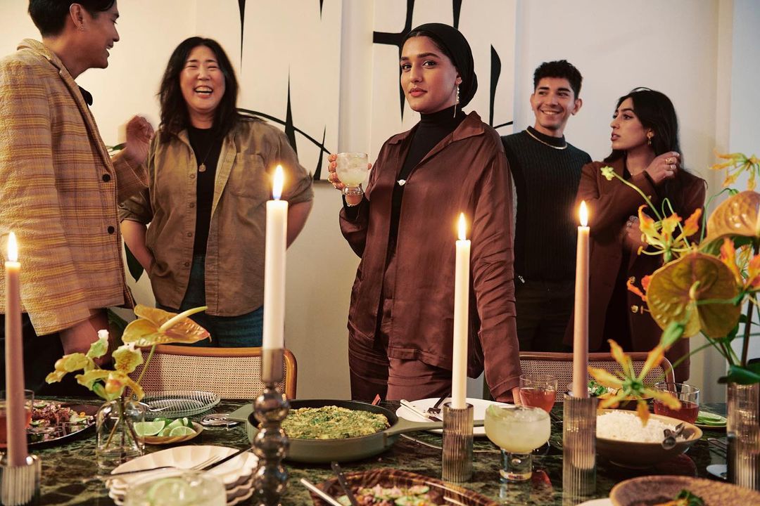 A group of five people gathered around a table with food and candles, creating a warm and inviting atmosphere for a social gathering.