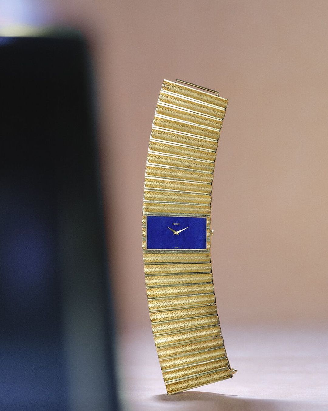 Elegant gold wristwatch with a striking blue rectangular face, showcased against a soft, neutral backdrop in a product-focused shot.