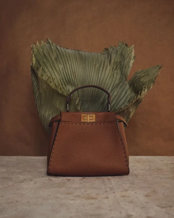 Brown leather Fendi Peekaboo handbag on a stone surface with a dried palm frond and a brown background in a studio setting.