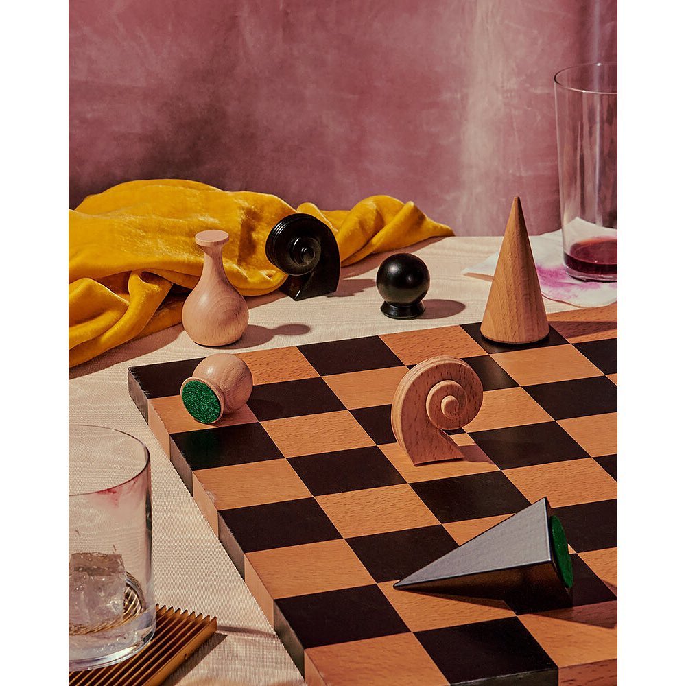 Chessboard with wooden chess pieces and a glass of red liquid in a studio setting, featuring a brown checkered board.