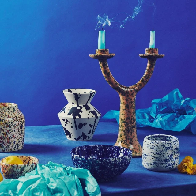 Still life studio shot on royal blue background of ceramic vases, bowls and candlestick with lit candles, smoke, and blue paper.