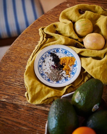 Overhead shot of turmeric, spices, and lemons arranged on a patterned plate, alongside avocados and citrus fruit on a wooden table.