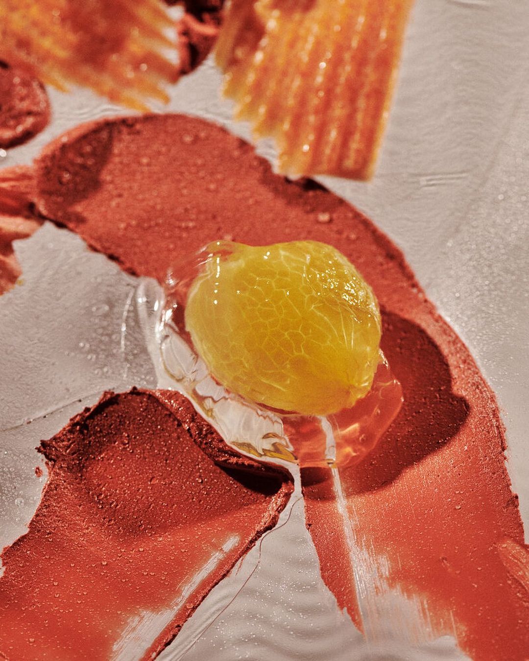 Close-up of a yellow food gel with red lipstick smears on a reflective surface, creating an abstract food and beauty-themed composition.