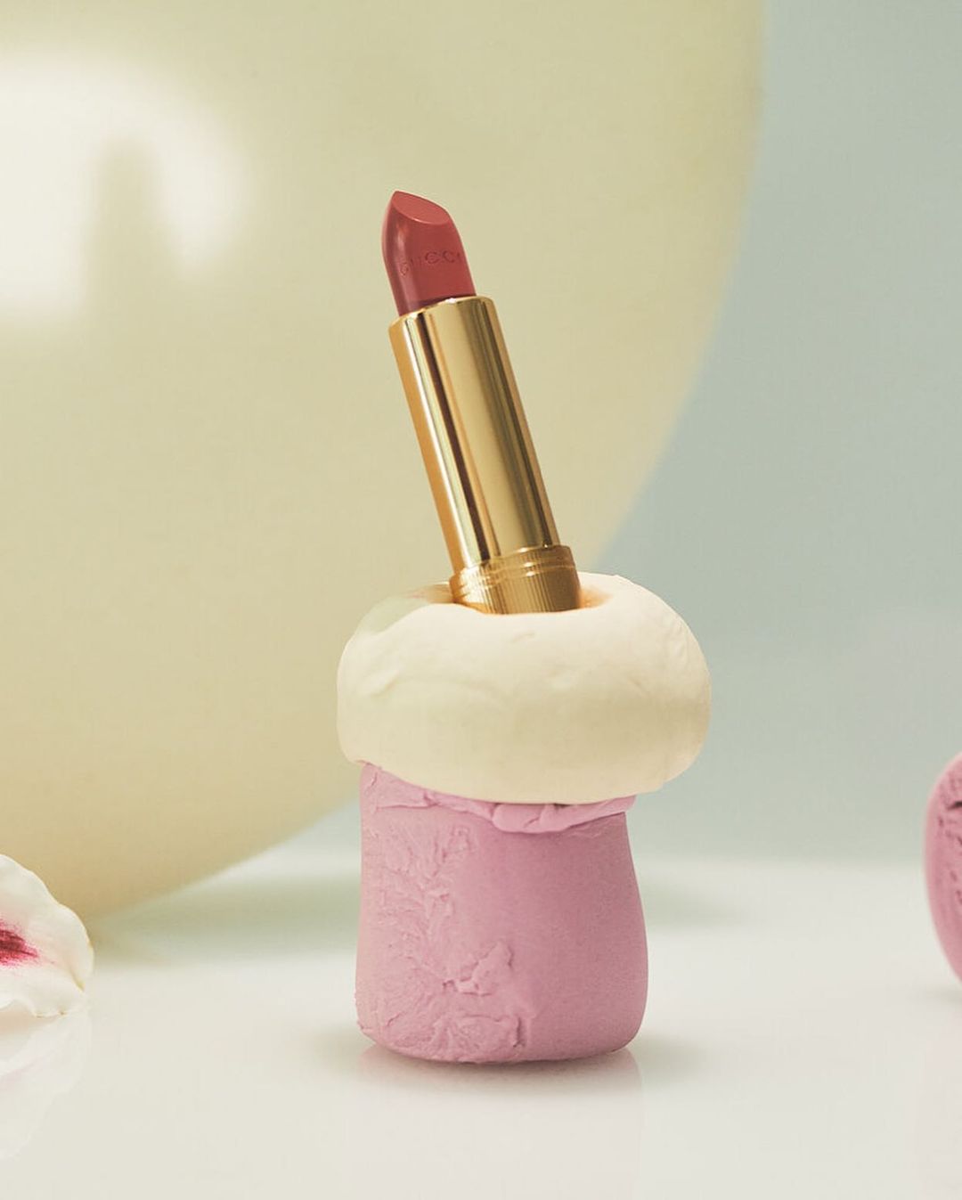 Close-up of a pink lipstick in a gold tube, presented in a decorative clay holder. Beauty shot for cosmetics and makeup.