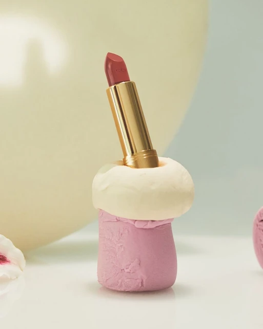 Close-up of a pink lipstick in a gold tube, presented in a decorative clay holder. Beauty shot for cosmetics and makeup.