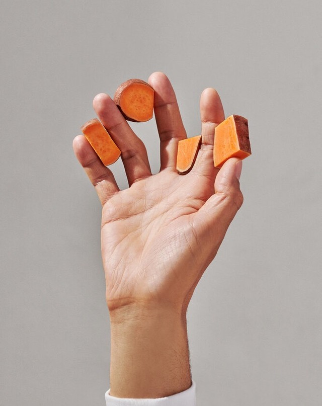 A hand holds five slices of vibrant orange sweet potato against a soft grey backdrop, capturing a fresh food still life.