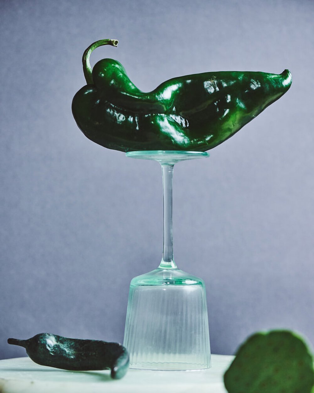 Poblano pepper resting on top of a glass cup, studio shot with soft lighting, and grey background for a minimalistic food still life.