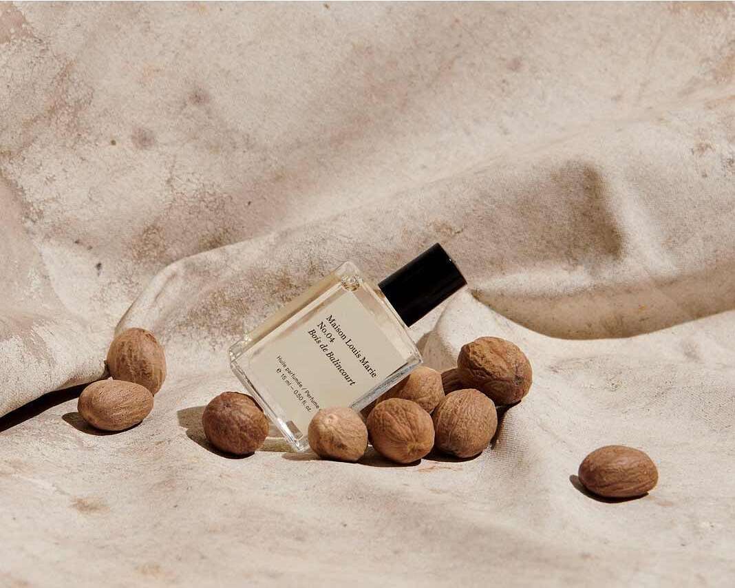 Still life shot of a perfume bottle next to pile of nuts on wrinkled fabric, featuring neutral color palette and a modern aesthetic.