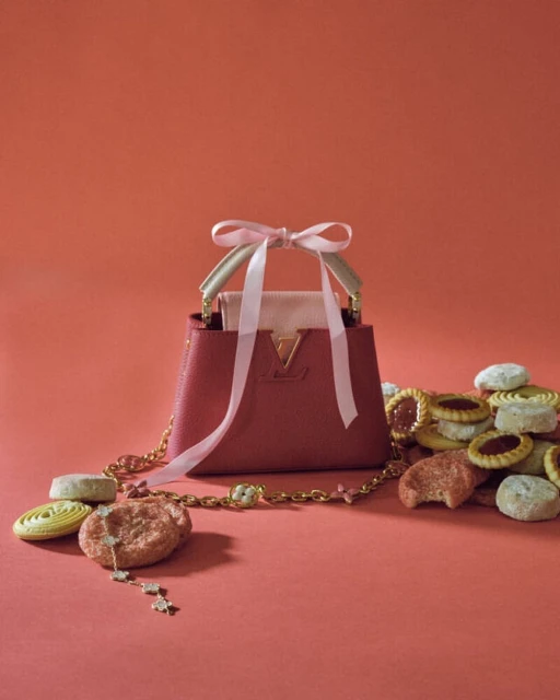 Designer handbag on a pink surface with sugar cookies. The bag features gold hardware, a small handle, and a pink ribbon.