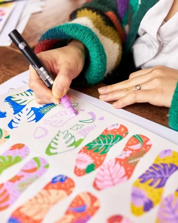 Adult hand drawing a tropical pattern with a marker. The artistic illustration is on a table indoors; colorful and detailed art.
