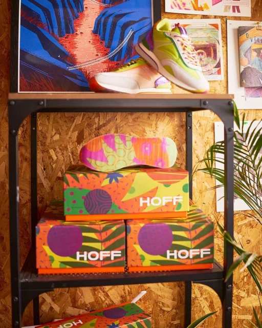 Colorful sneakers displayed on a black metal shelf along with patterned boxes and art prints creating a vibrant, eye-catching composition.