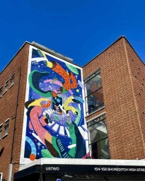 Large colourful mural painted on a brick building exterior in London under a clear blue sky