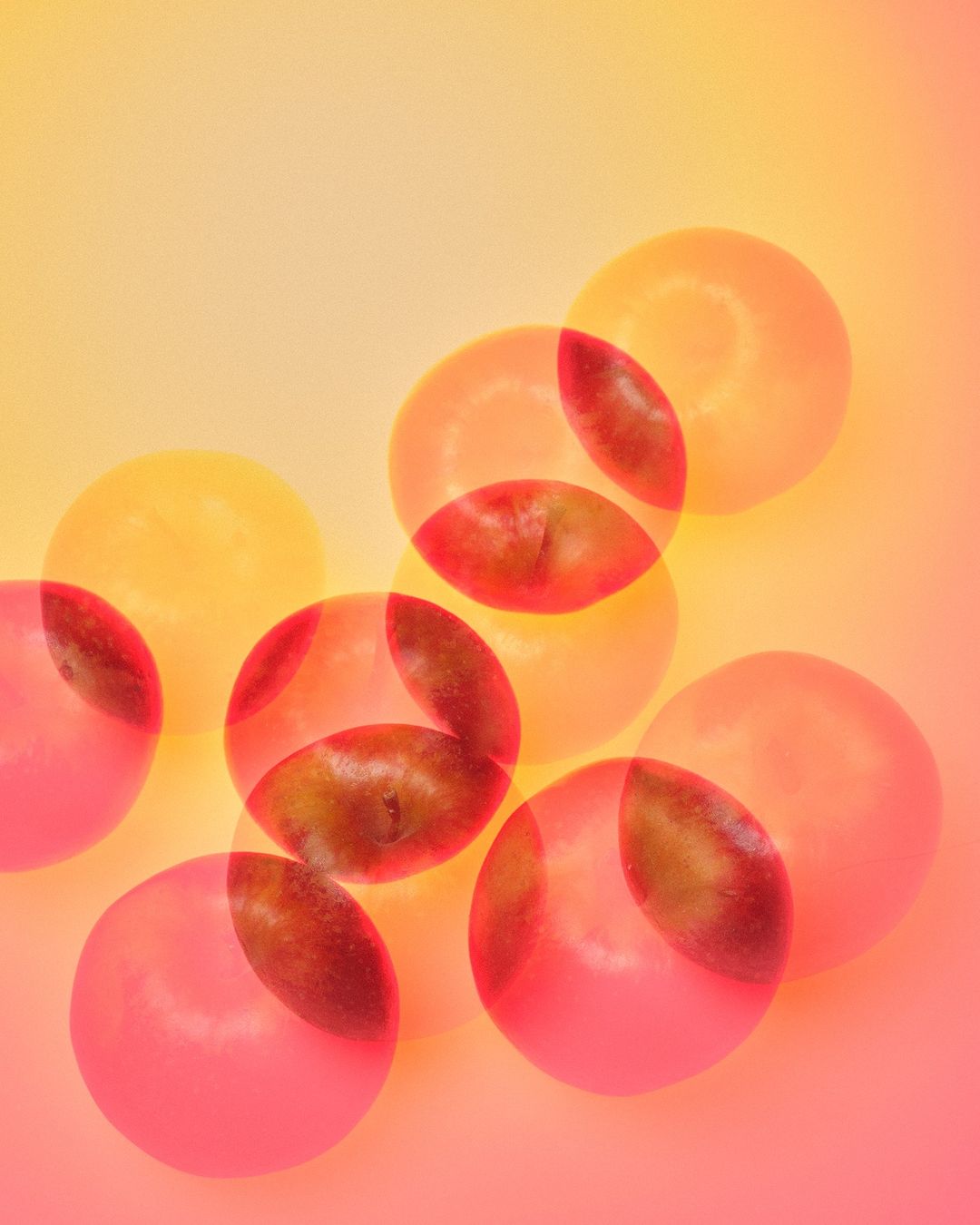 Overlapping semi-transparent grapes in shades of orange, pink, and red on a warm-toned gradient background create a playful, abstract composition.